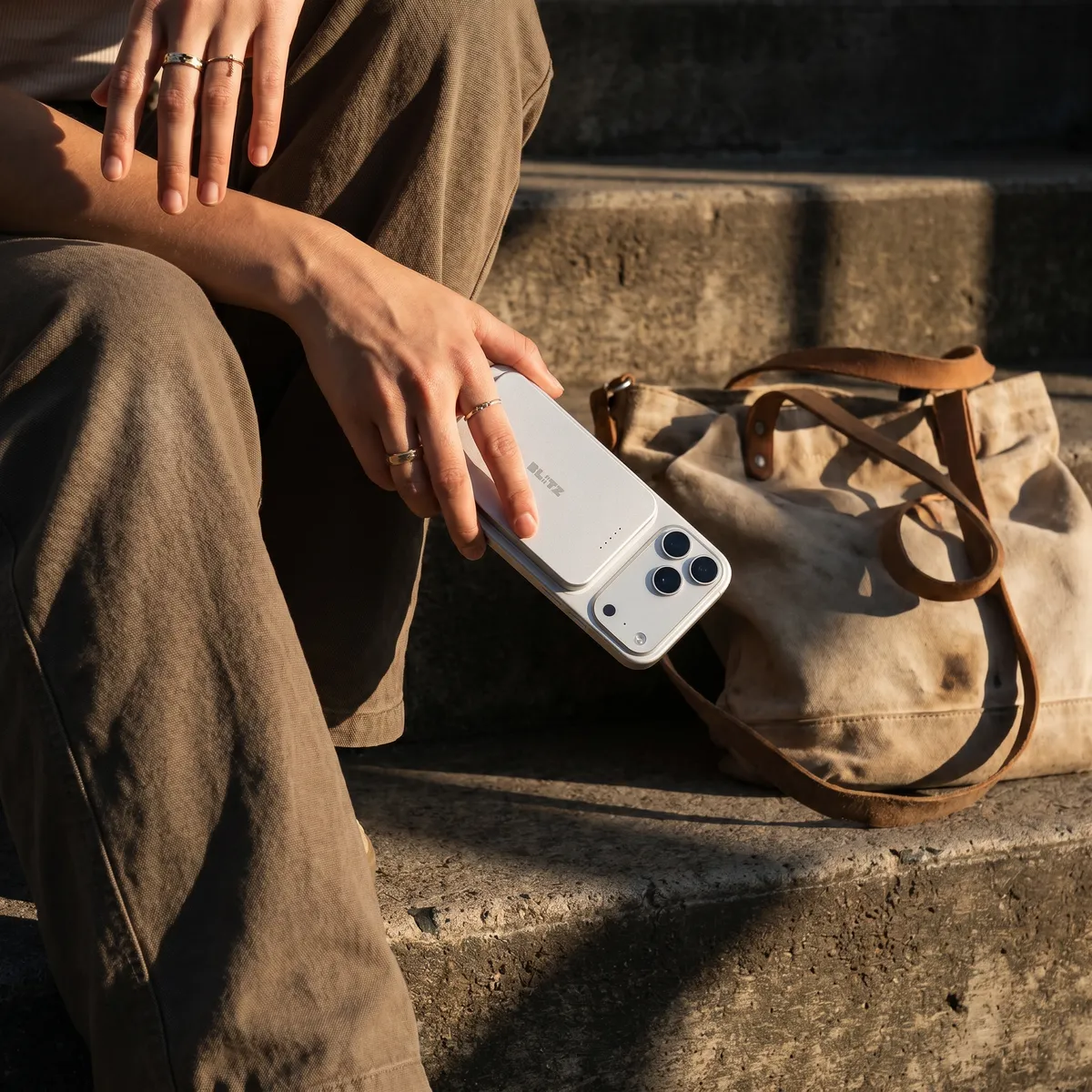 Person on stone steps holding a phone with the silver power bank, a canvas bag beside them