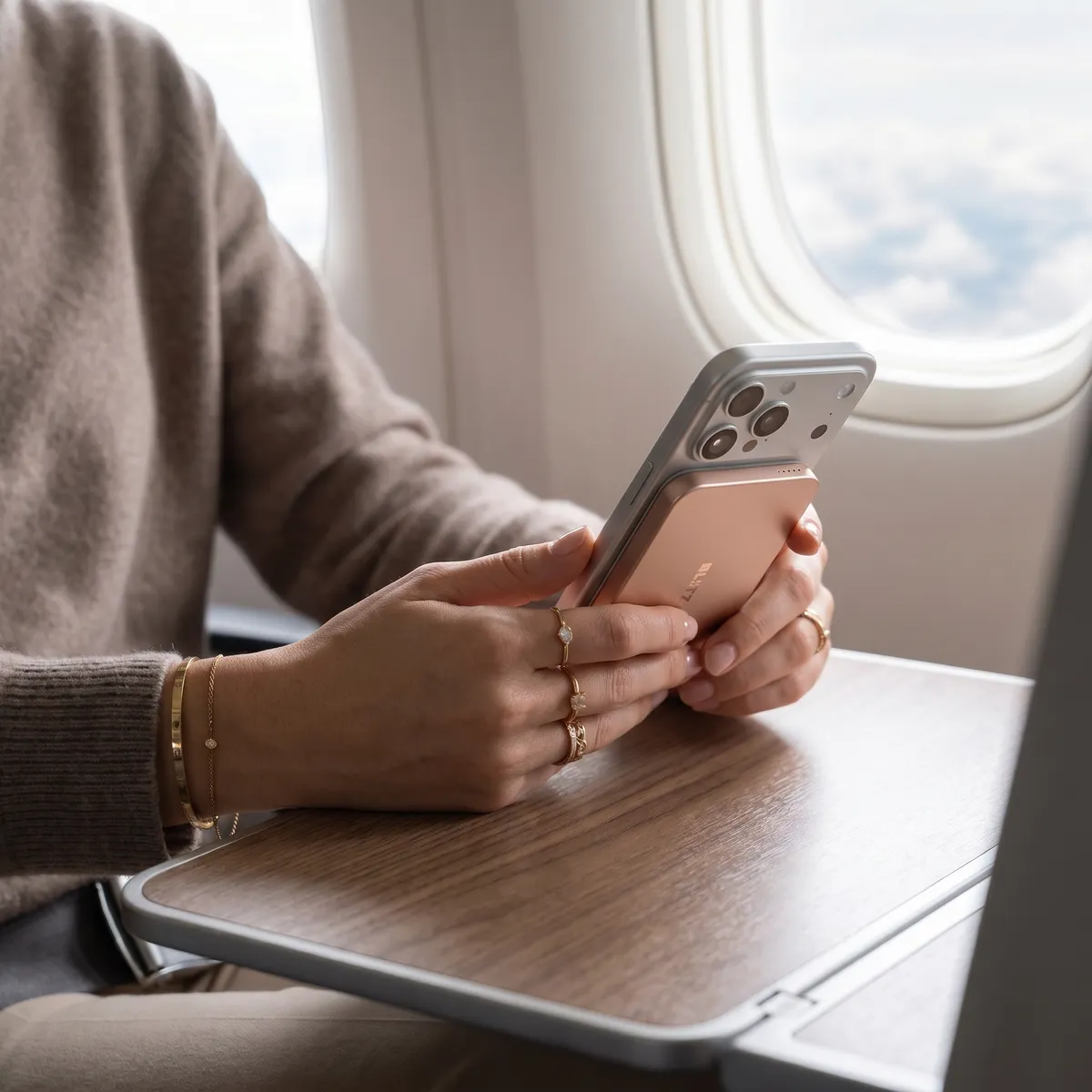 Hands holding a phone with the power bank above an airplane tray table